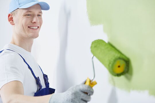 Ein glücklicher Mann streicht die Wand in der Farbe grün 